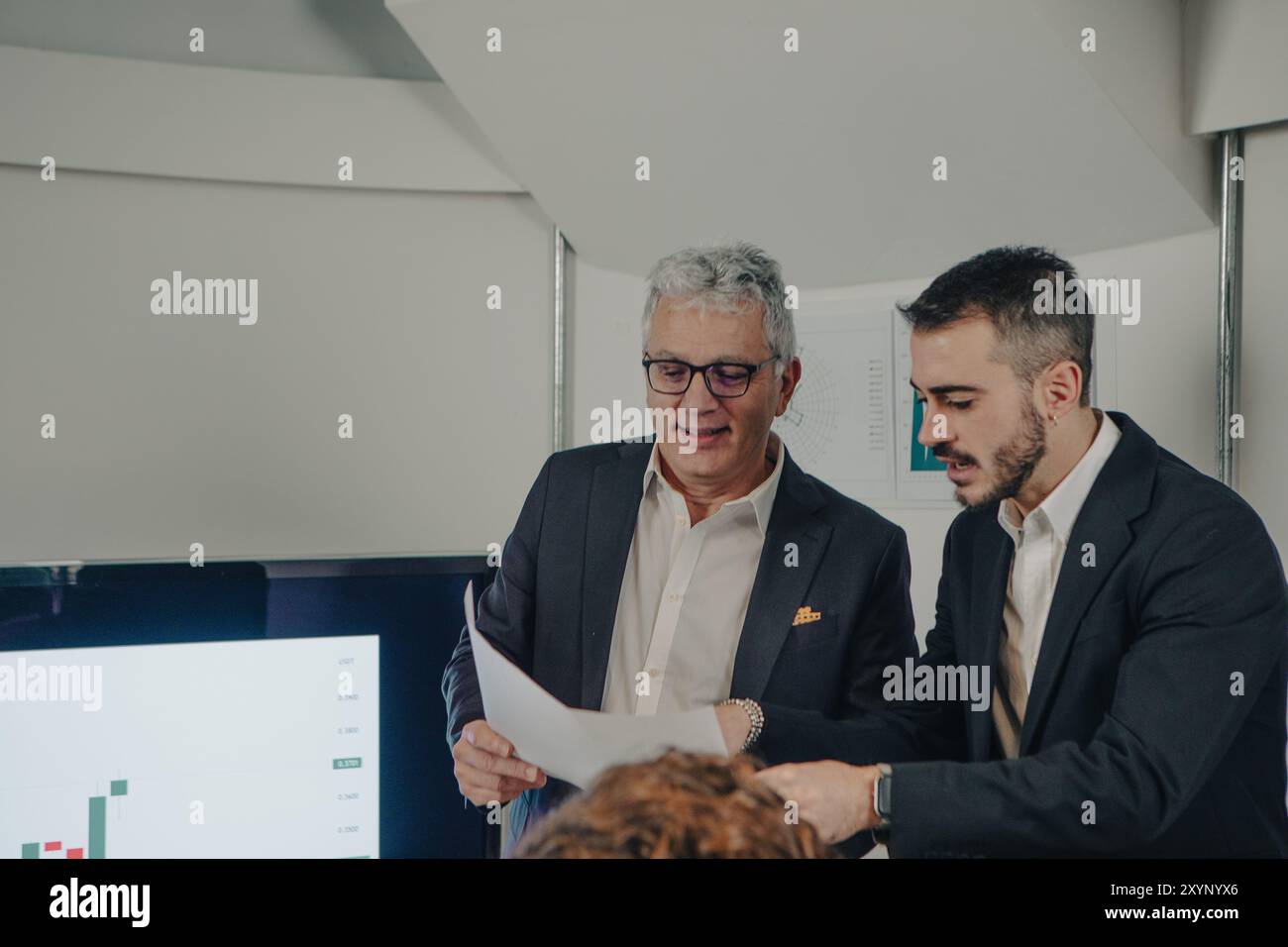 Two businessmen having a discussion about some documents while analyzing charts on a screen Stock Photo