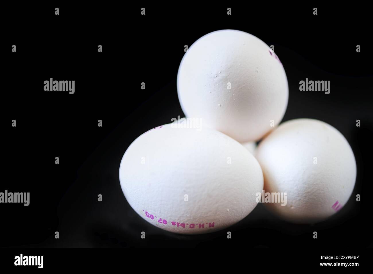 4 white chicken eggs against a black background Stock Photo