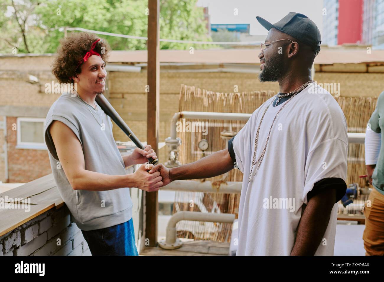 Curly haired man leaning on bricks while greeting his buddy in backyard Stock Photo