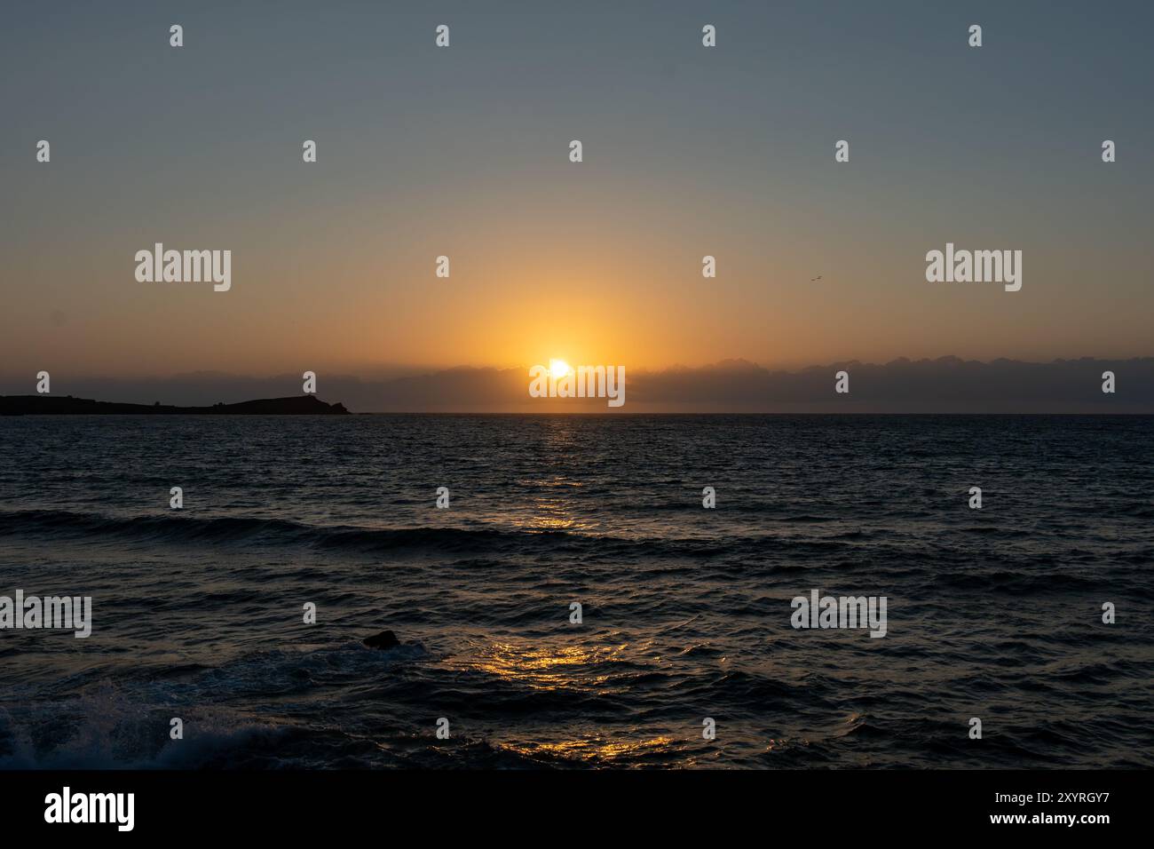 The sun setting on the horizon, casting a warm glow over the ocean in ...