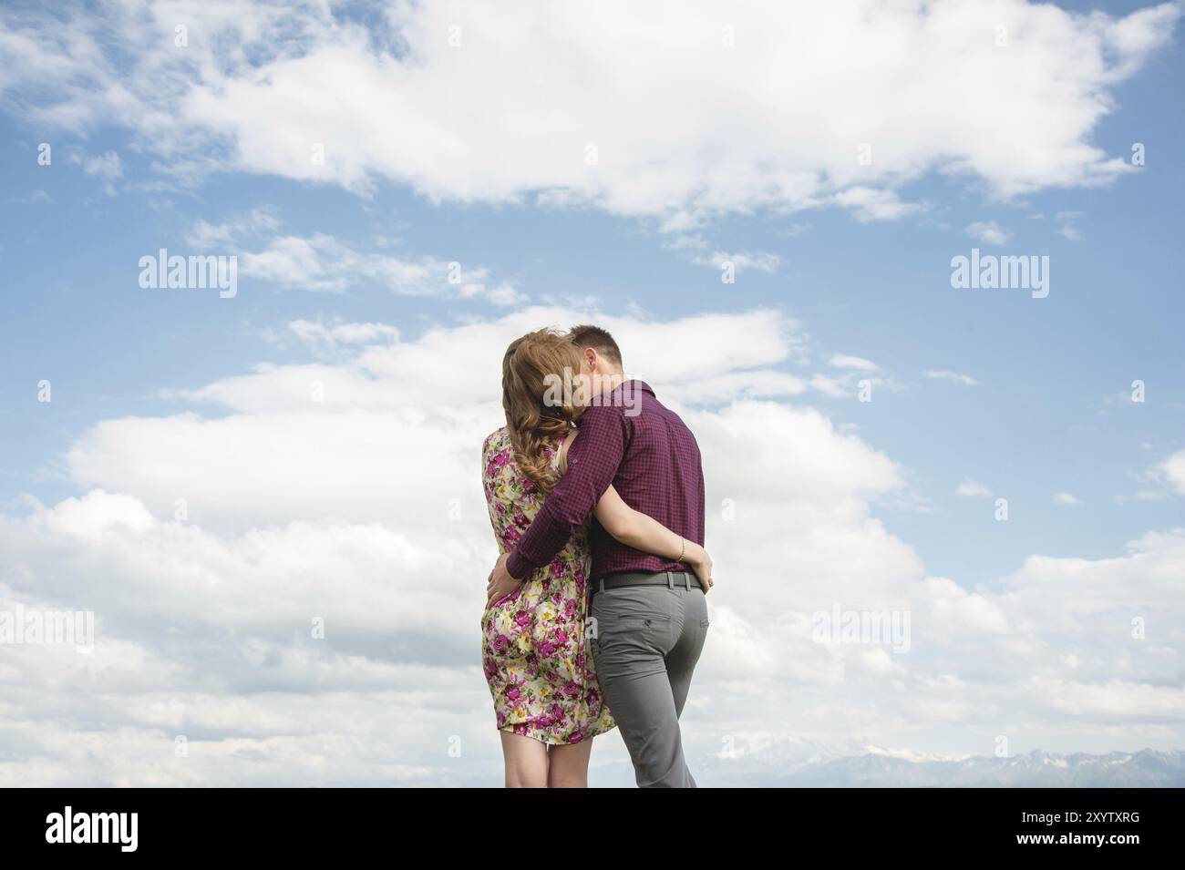 View from the back. Young couple hugging kisses against the blue sky and white clouds. The concept of ideal relations and family Stock Photo