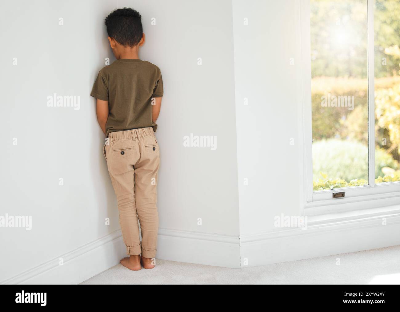 Back, child and sad in corner for discipline, behavior development and time out at home. Punishment, naughty kid and stand at wall for domestic abuse Stock Photo