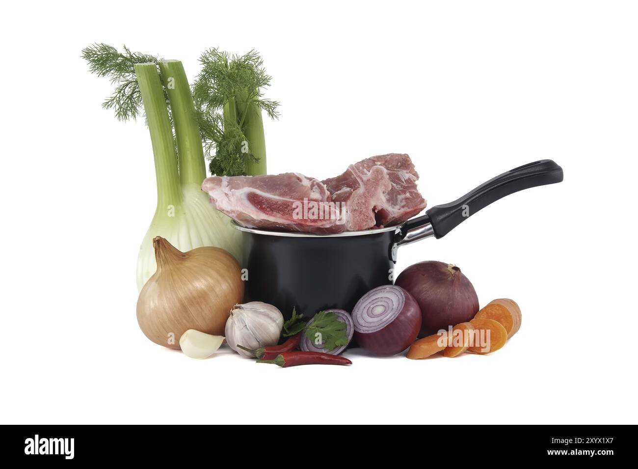 Black saucepan with pieces of raw pork atop. Around the saucepan are sliced vegetables which include onions, carrots, and garlic isolated on white bac Stock Photo