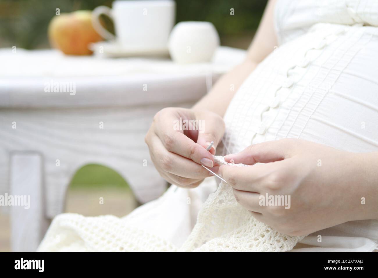 Pregnant young woman in white knitting in the garden Stock Photo - Alamy