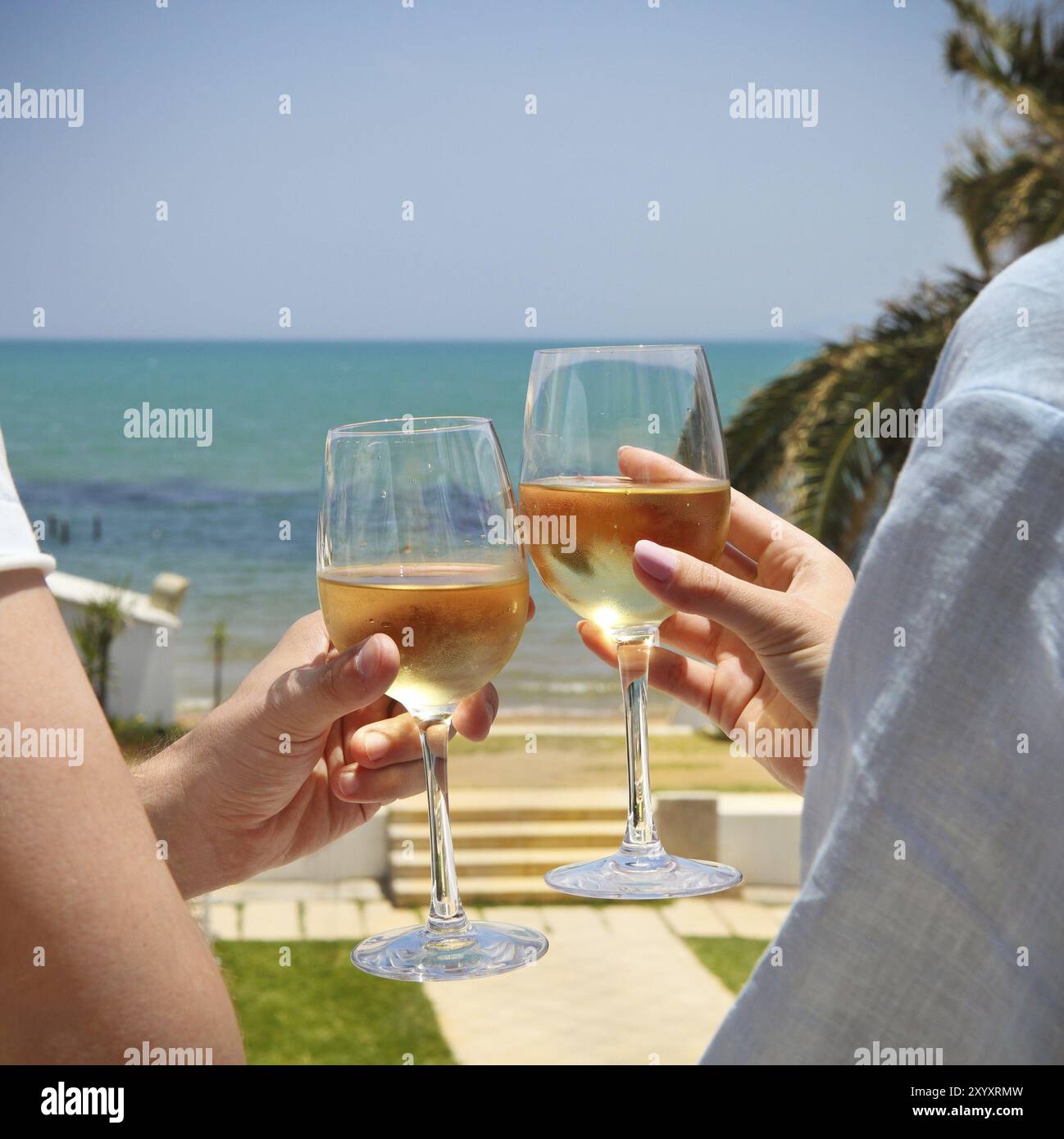 Man and woman clanging wine glasses with white wine at sky and sea ...