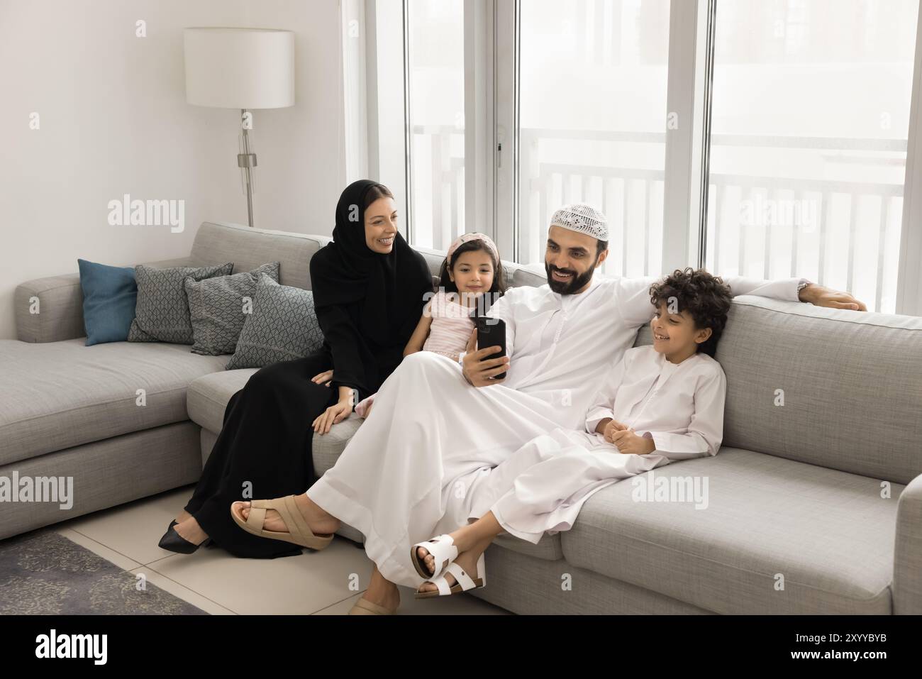 Happy Arabic parents and two little children using smartphone together ...
