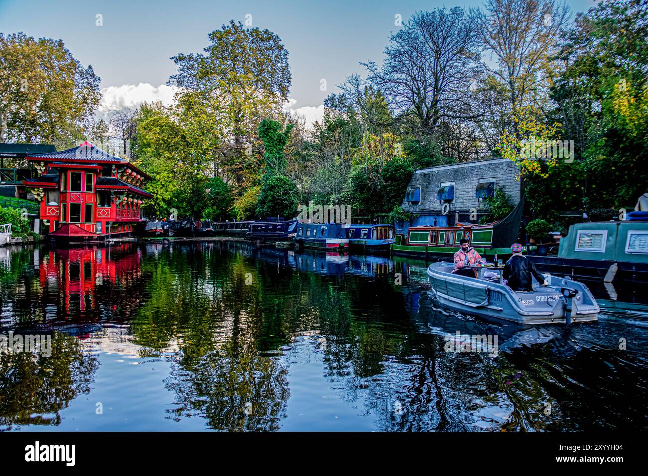 Beautiful view of Regent's Canal in London: a floating Chinese restaurant, small boats around and two friends on a boat enjoying a peaceful picnic. Stock Photo
