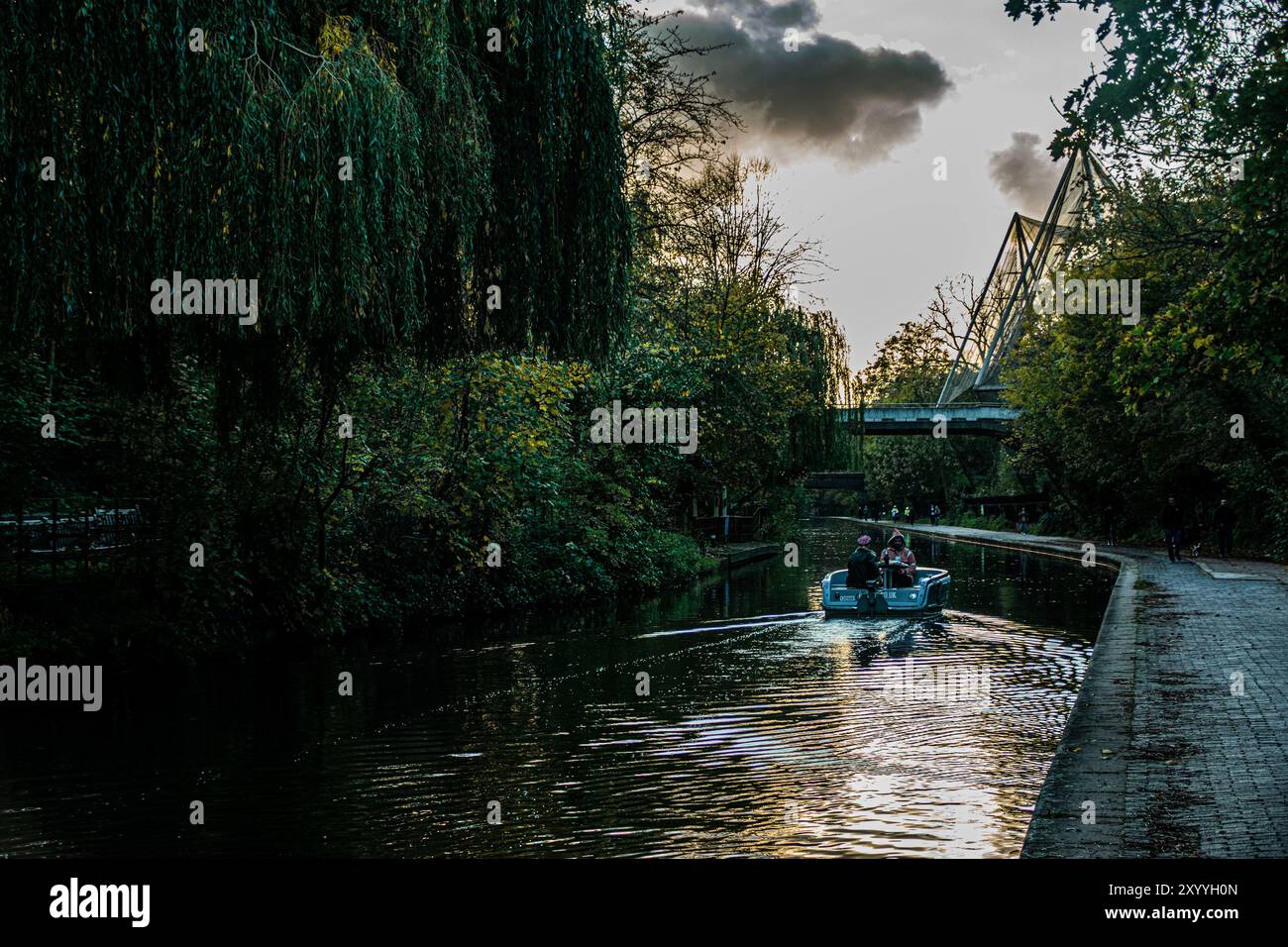 A peaceful boat ride along Regent's Canal at dusk, surrounded by lush greenery and soft reflections, offering a tranquil escape in the heart of London. Stock Photo