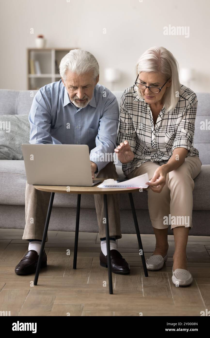 Serious older spouses pay household bills using laptop Stock Photo