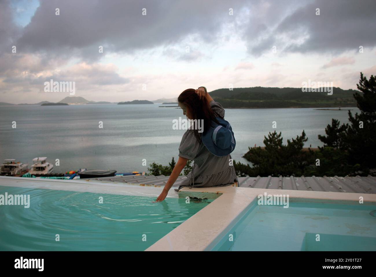 Dolsan-eup, Yeosu-si, South Korea - July 26, 2024: Young woman watching sunrise at a resort with a swimming pool overlooking the sea in Yeosu Stock Photo