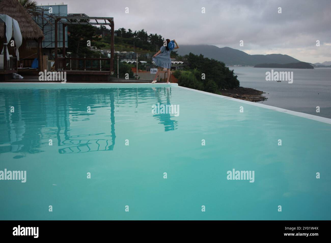 Dolsan-eup, Yeosu-si, South Korea - July 26, 2024: Young woman watching sunrise at a resort with a swimming pool overlooking the sea in Yeosu Stock Photo