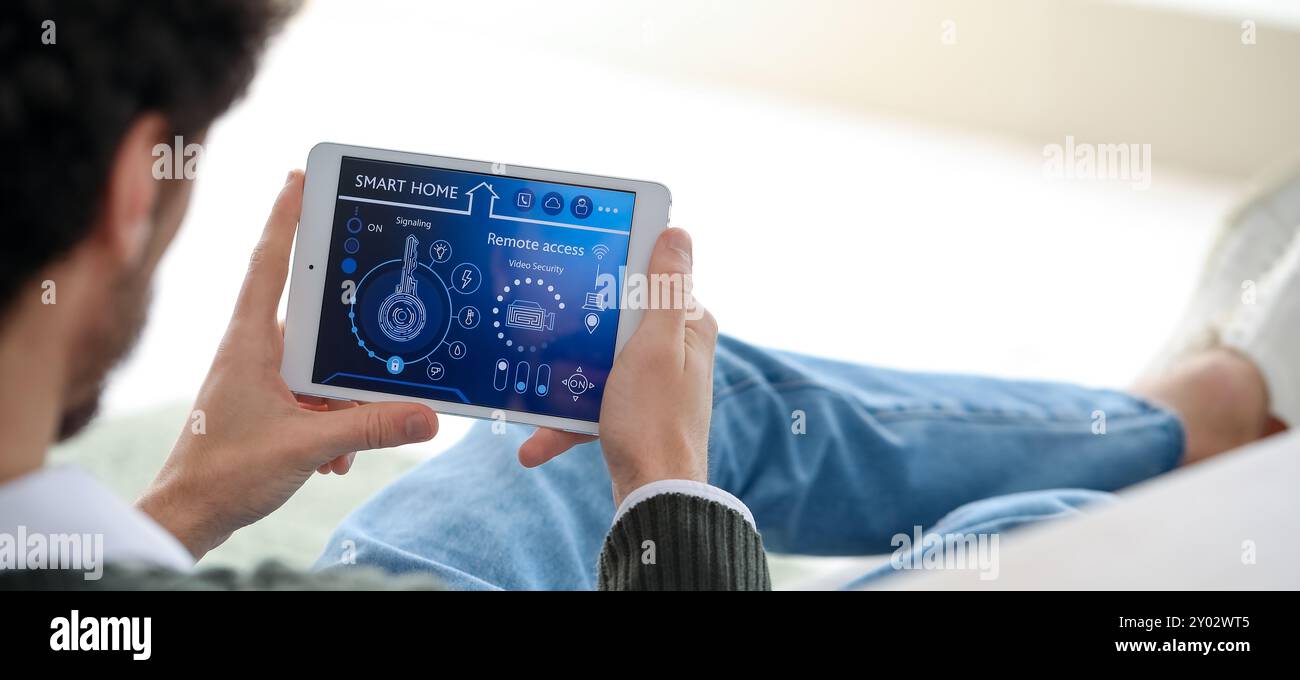 Young man holding tablet computer with smart home security system on screen Stock Photo