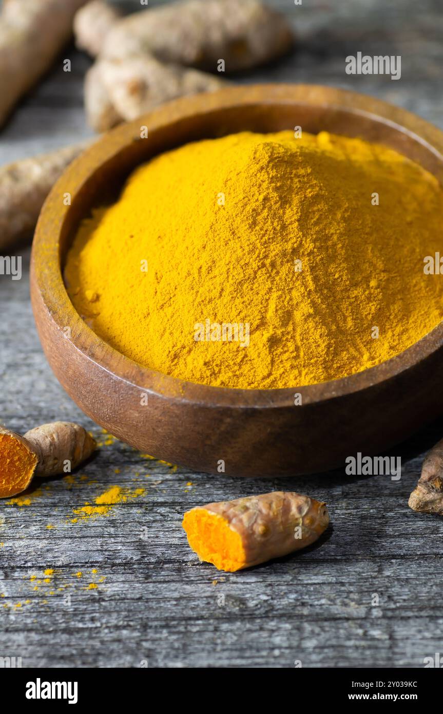 Turmeric powder in spoon or bowl and fresh turmeric root on wooden background, spice concept, ( curcuma longa ) Stock Photo