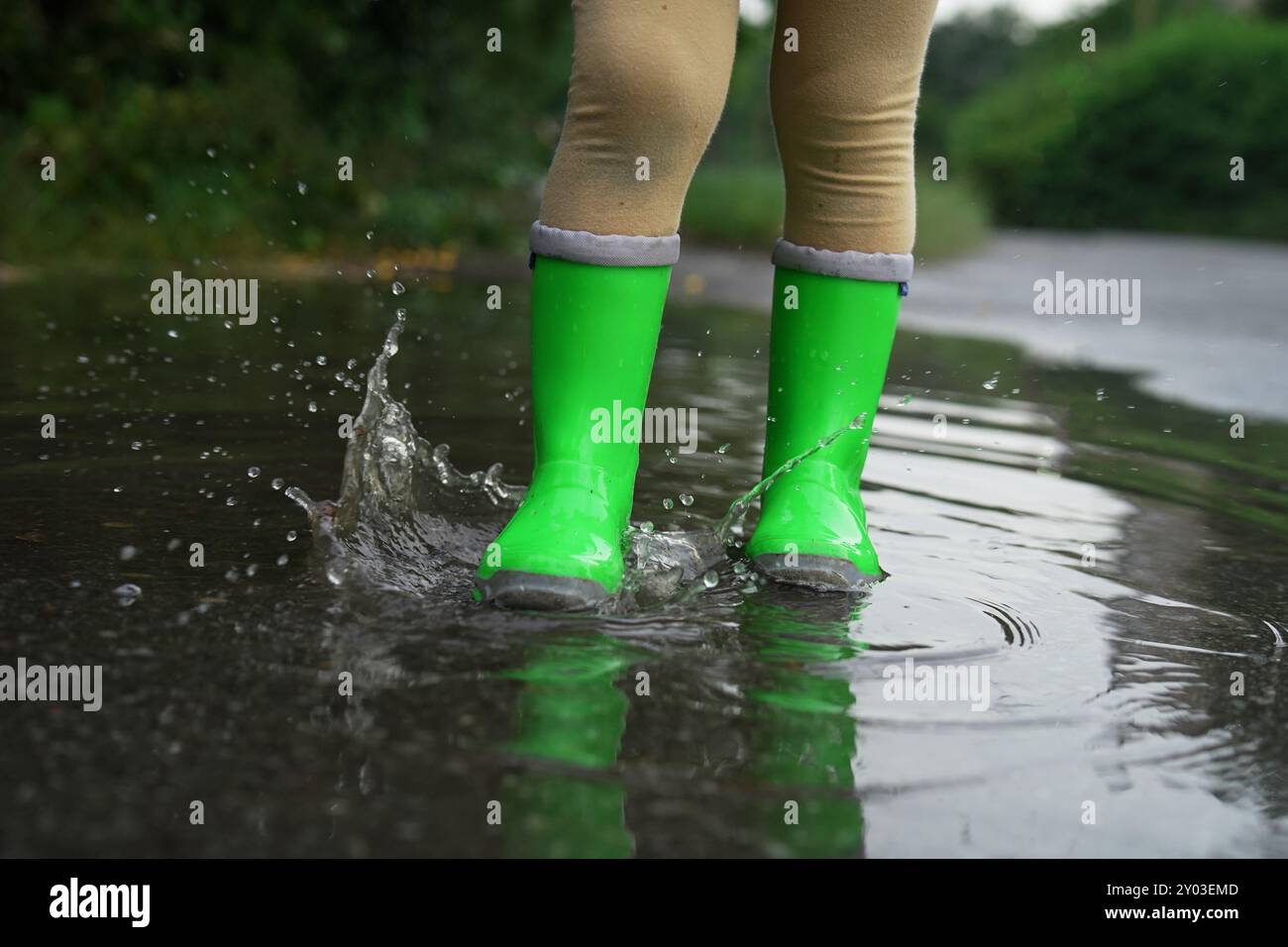 Little girl wearing green rubber boots walking in puddle outdoors ...