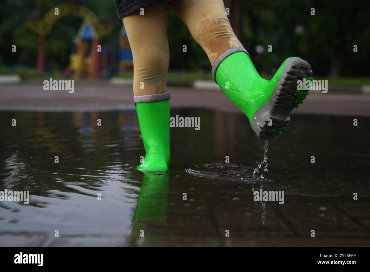 Little girl wearing green rubber boots walking in puddle outdoors ...