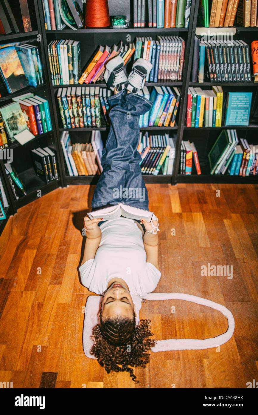 High angle view of woman reading book while lying down with feet up on shelf in bookstore Stock Photo