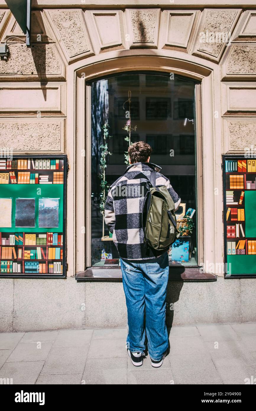 Rear view of man with backpack standing near window of bookstore Stock Photo