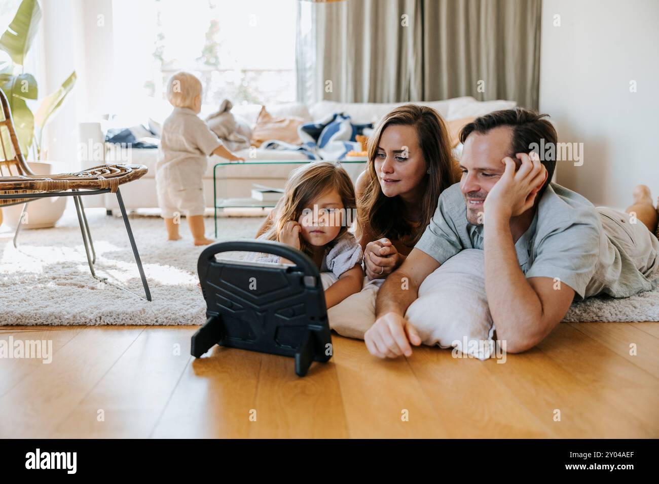 Father and mother watching tablet PC while lying down with daughter on floor at home Stock Photo