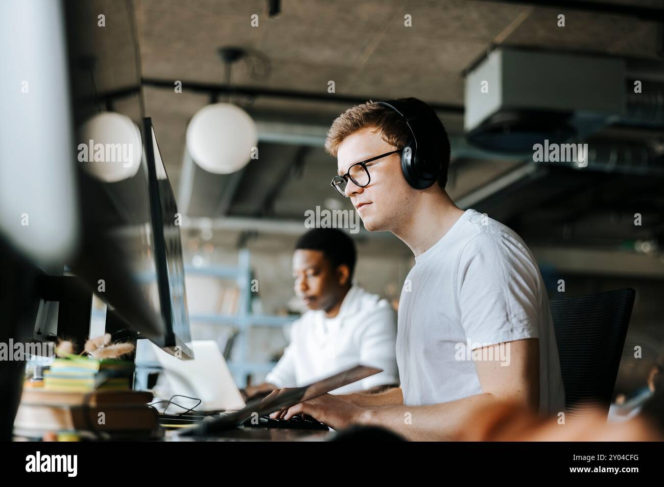 Young male programmer doing coding on computer with wireless headphones in office Stock Photo