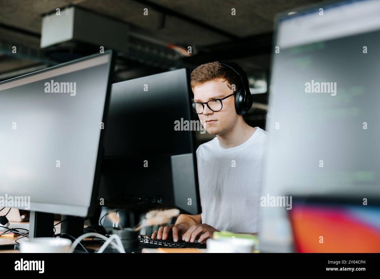 Young male computer programmer typing on desktop PC while sitting on desk in office Stock Photo