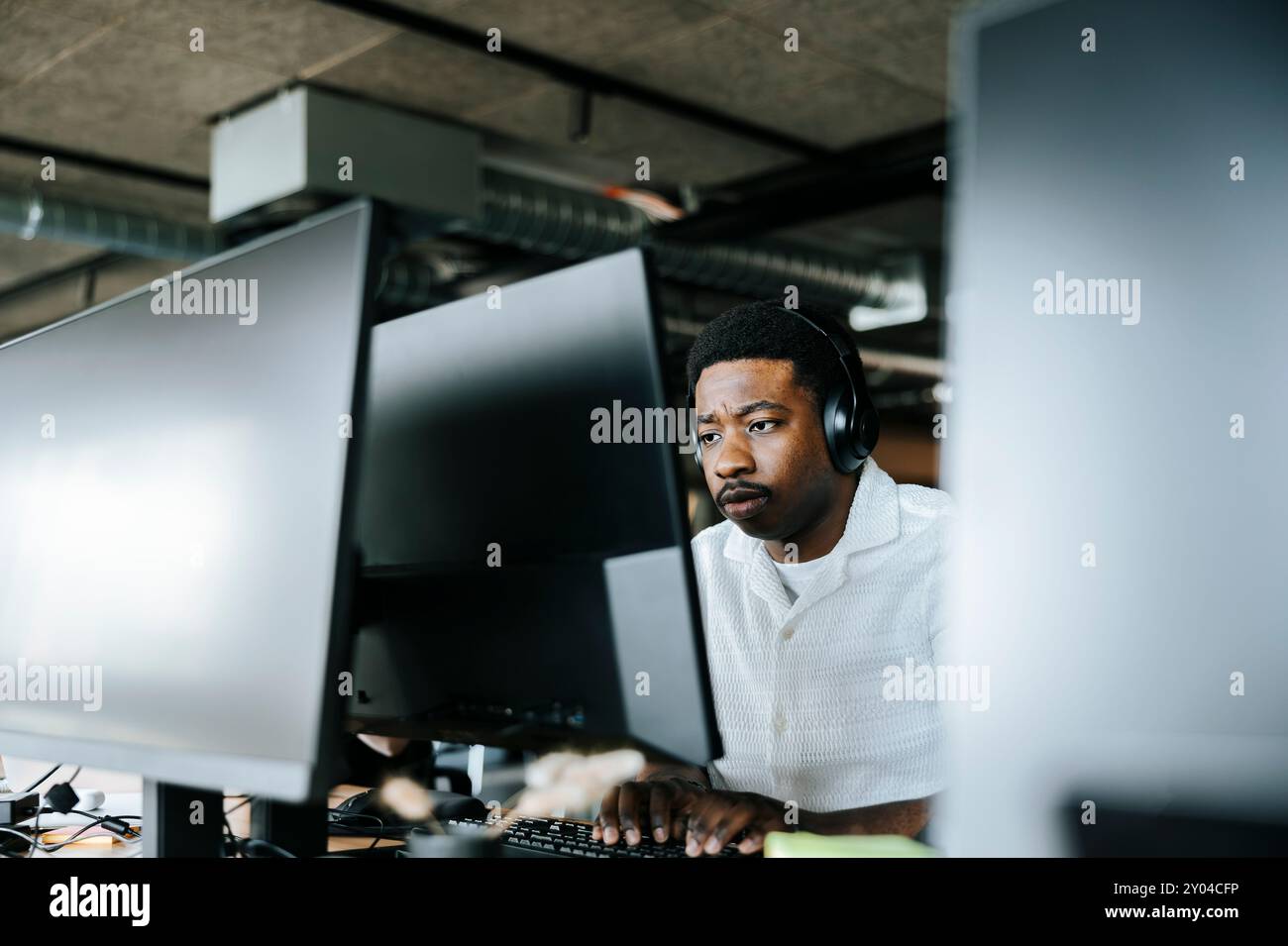 Focused young businessman with wireless headphones doing coding on computer at office Stock Photo
