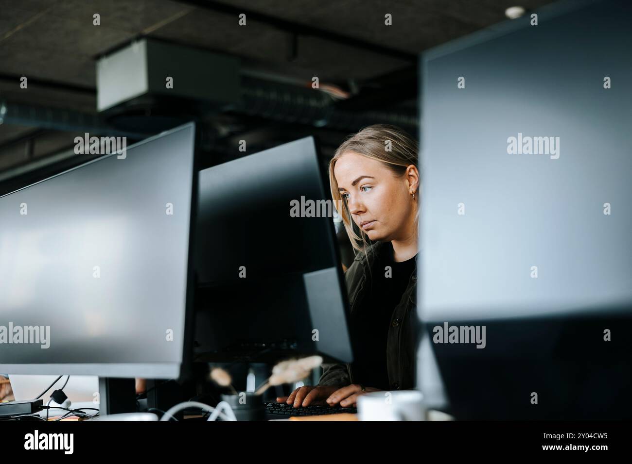 Focused female programmer doing coding on computer while sitting at desk in office Stock Photo