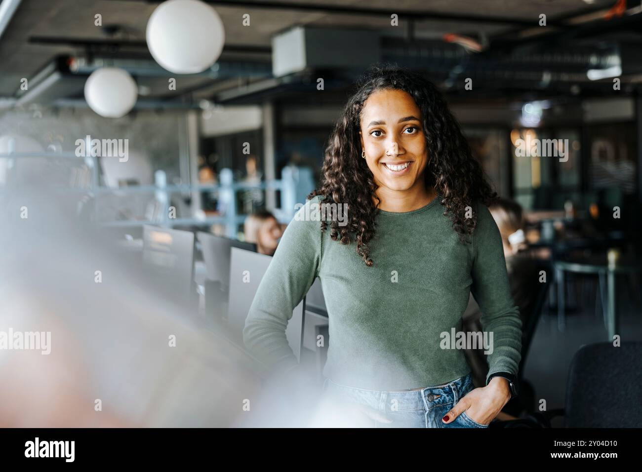 Portrait of happy female programmer with hands in pockets standing in tech startup office Stock Photo