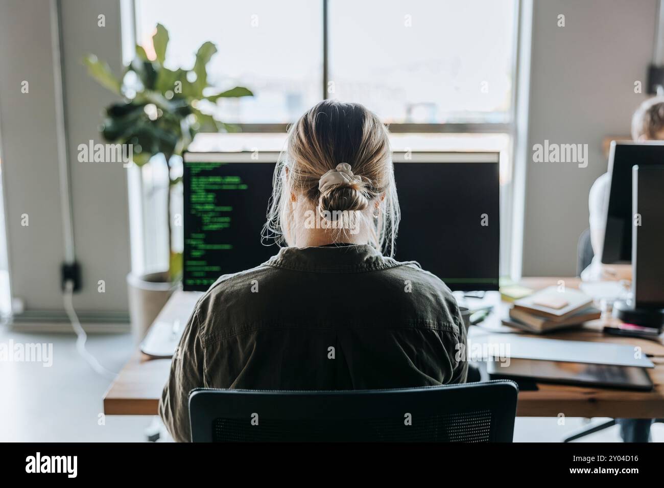 Rear view of female programmer coding on computer while sitting at desk in office Stock Photo