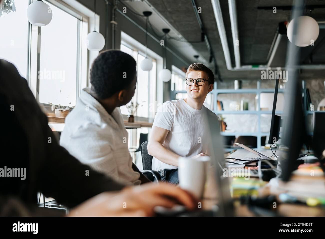 Male programmer talking with colleague while working in tech startup office Stock Photo