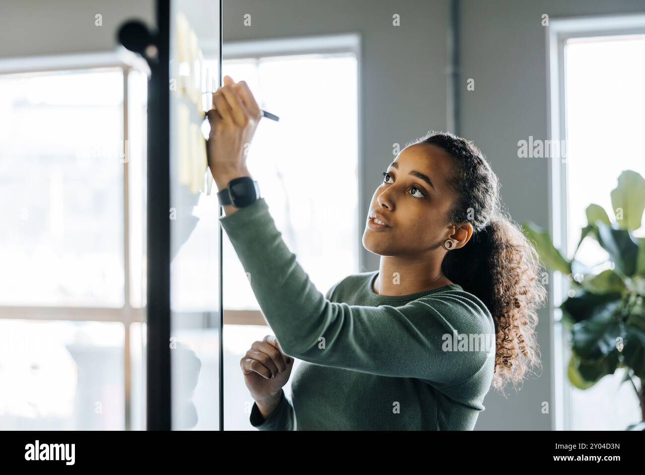 Young female tech programmer writing ideas on whiteboard in office Stock Photo
