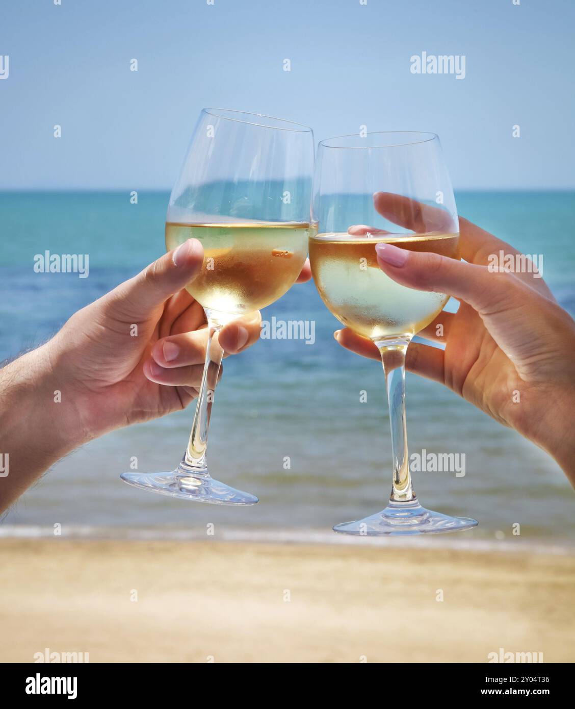 Man and woman clanging wine glasses with white wine at sky and sea ...