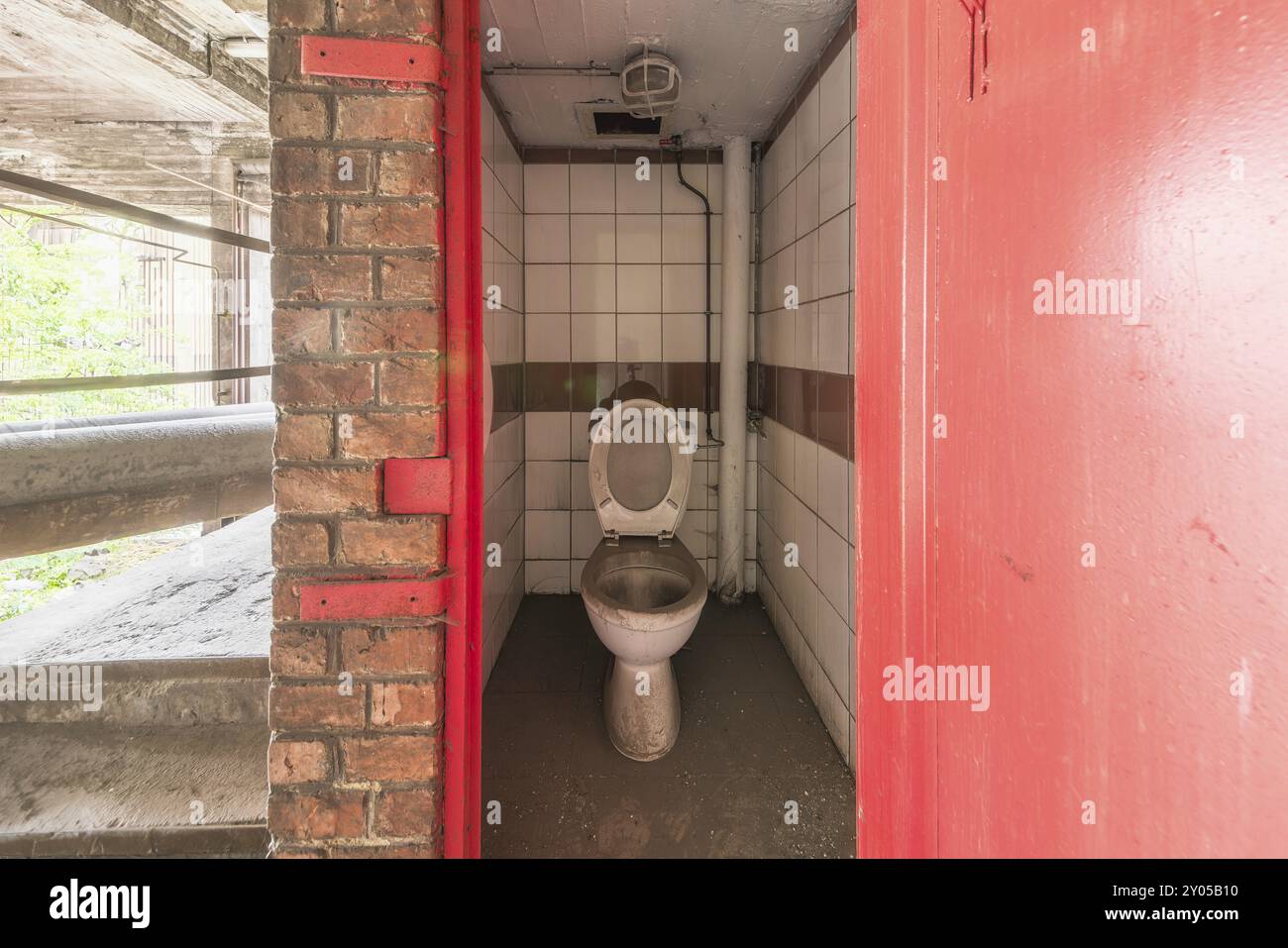 Abandoned toilet with red walls and tiles, visibly unused, steelworks