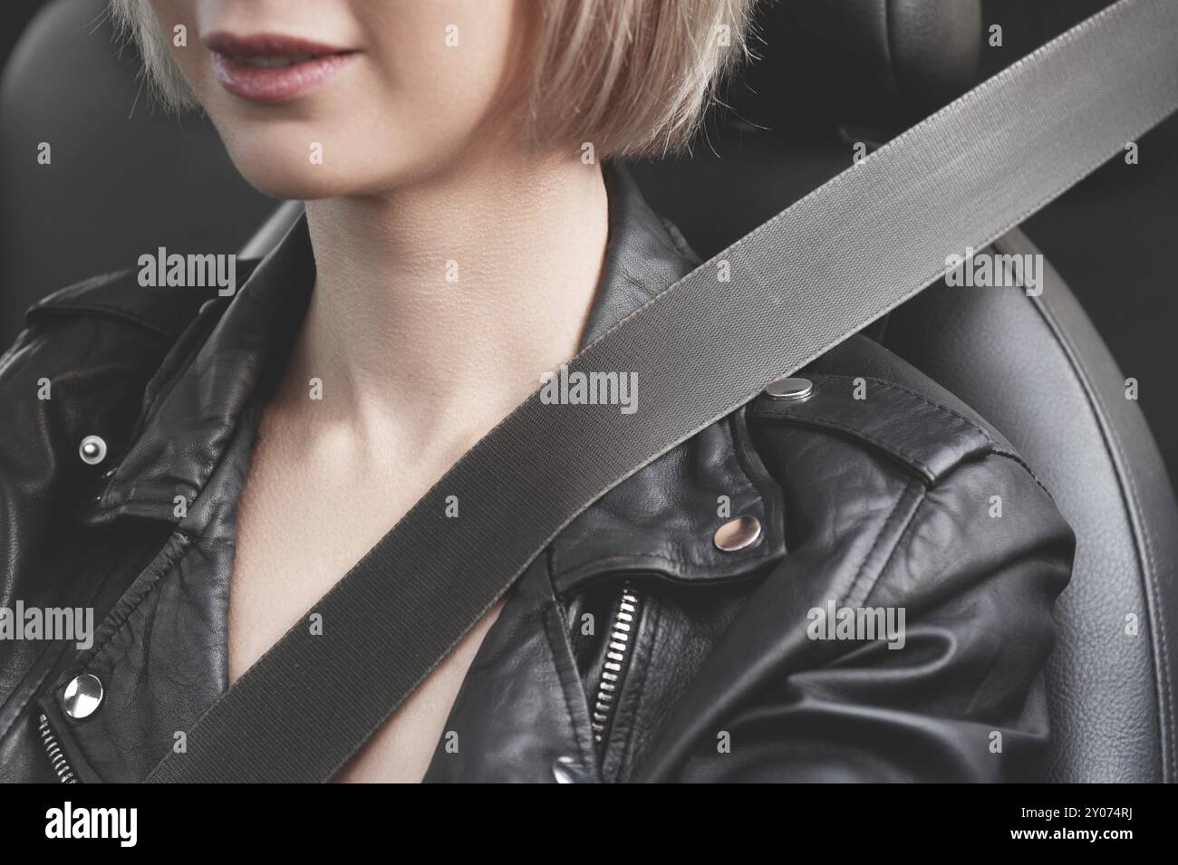 A close-up of a young hipster girl in a leather jacket in a car fastened with a seat belt. The concept of safety and protection of the driver on the r Stock Photo