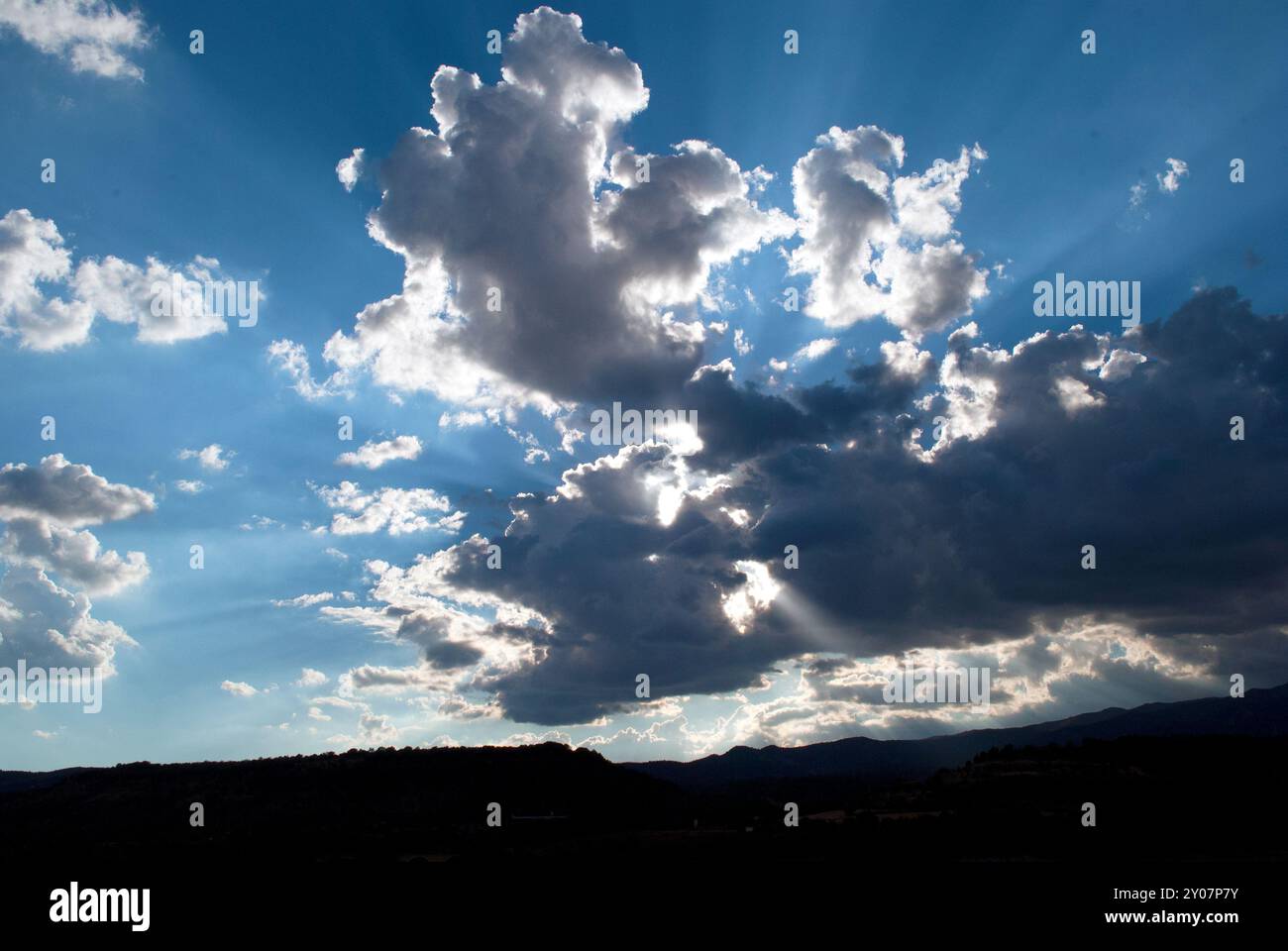 Gray and white clouds partially cover the sun at sunset, with a blue sky in the background creating a soft, moody atmosphere. Stock Photo