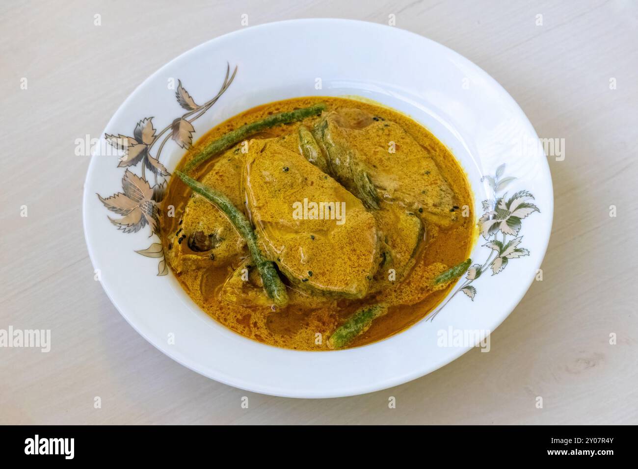 Tasty shorshe ilish on a white plate on a light wooden surface. This recipe is made from Hilsa fish (Tenualosa ilisha). Traditional Bengali cuisine co Stock Photo