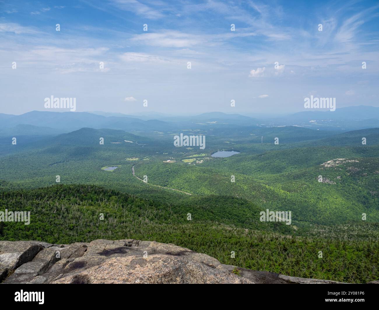 Breathtaking view from the summit of Cascade Mountain, with a rugged rock foreground and the Olympic Ski Jumping complex visible in the distance in La Stock Photo