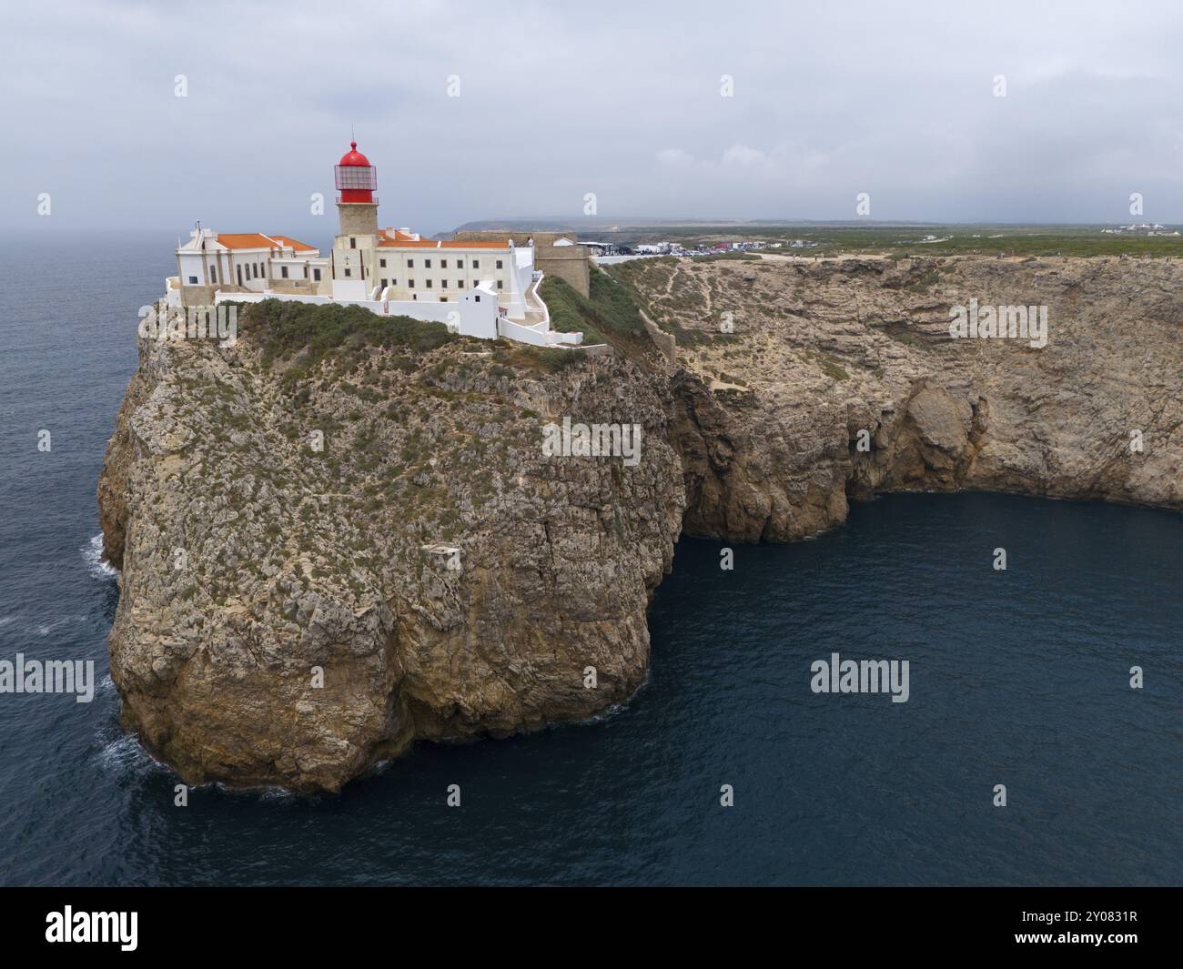 A red lighthouse and white buildings stand on an imposing cliff with a ...