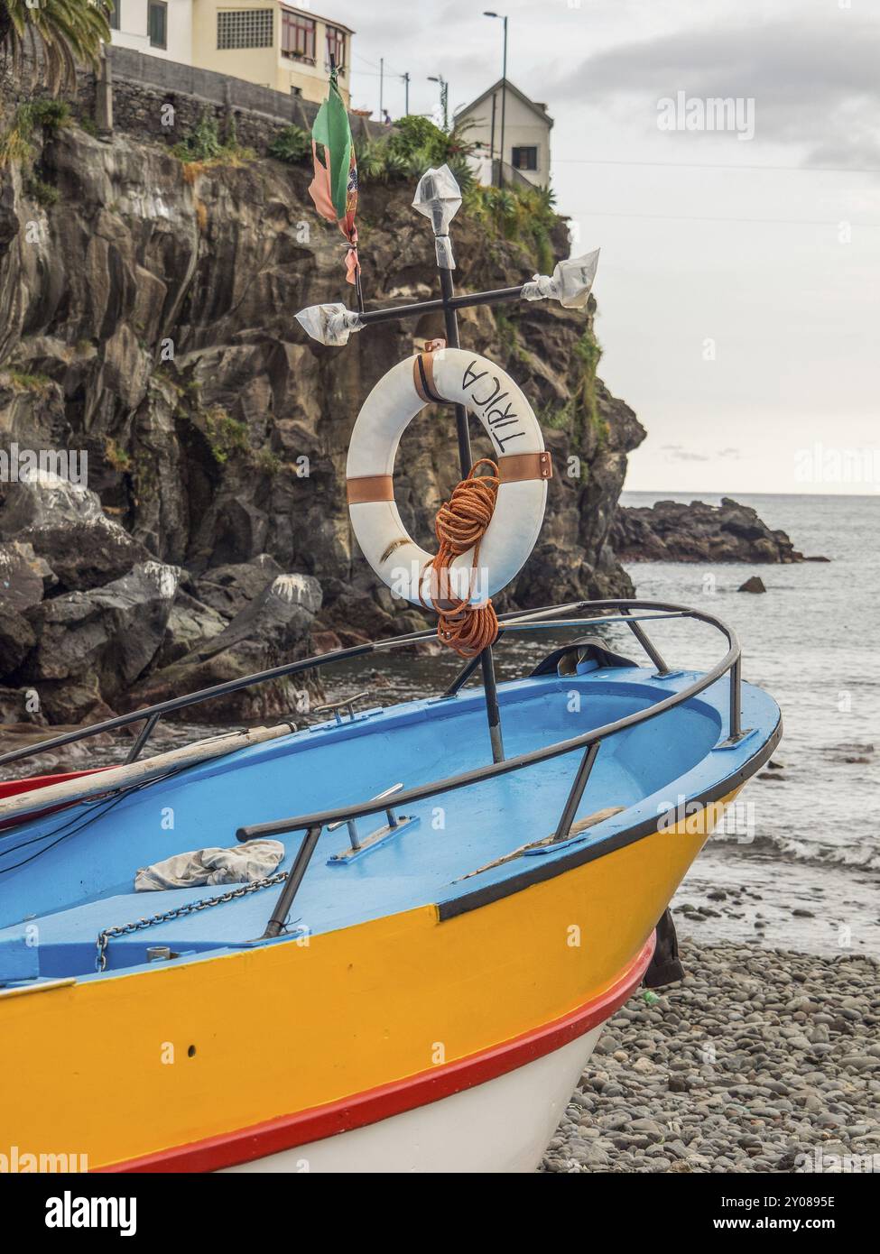 A colourful fishing boat with lifebuoys on a rocky shore next to the sea, Funchal, madeira, portugal Stock Photo