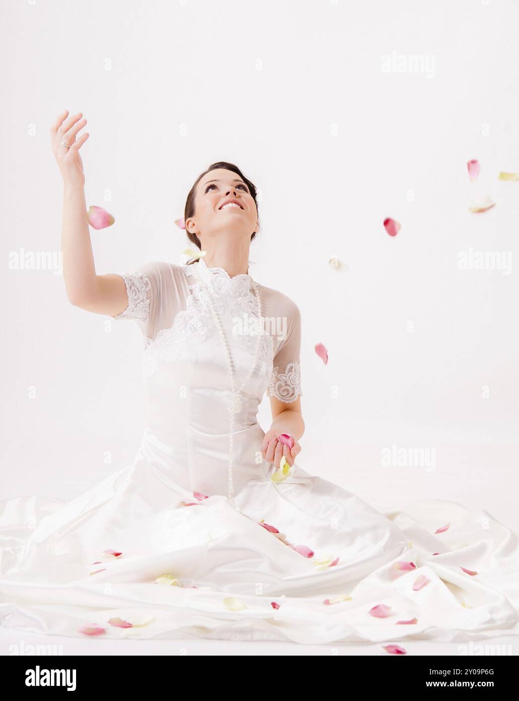 Pretty woman in an elegant white dress throws rose petals in the air ...