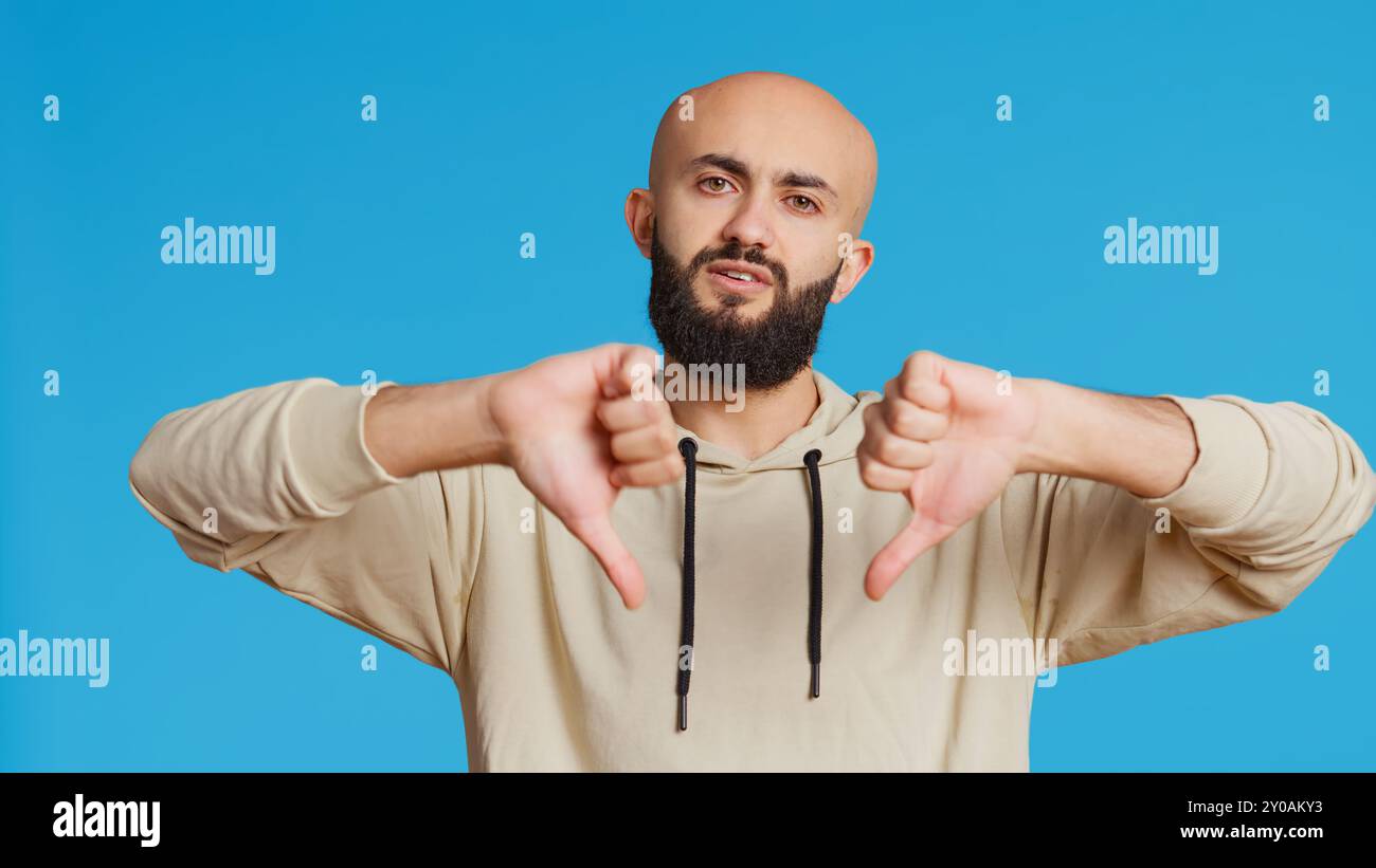 Middle eastern guy showing thumbs down sign on camera, giving dislike ...