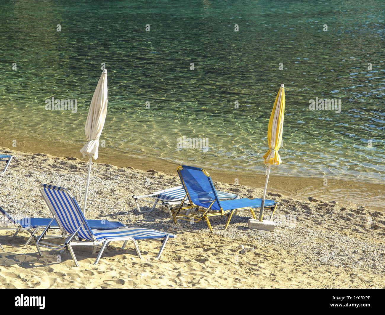 A sandy beach with blue sun loungers and parasols in clear, calm waters, corfu, mediterranean sea, greece Stock Photo