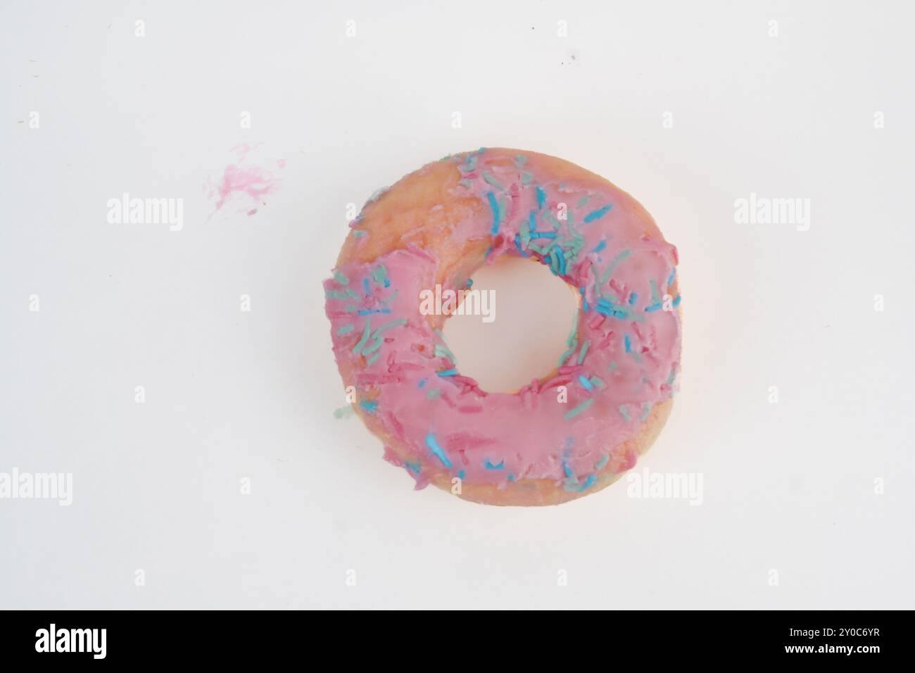 A pink donut with sprinkles on top. The donut is sitting on an isolated white background. Stock Photo