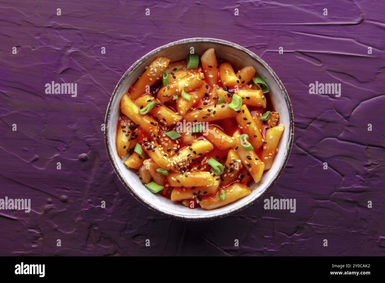 Tteokbokki or topokki, Korean street food, spicy rice cakes in red pepper gochujang sauce, overhead flat lay shot on a purple background, Food photogr Stock Photo