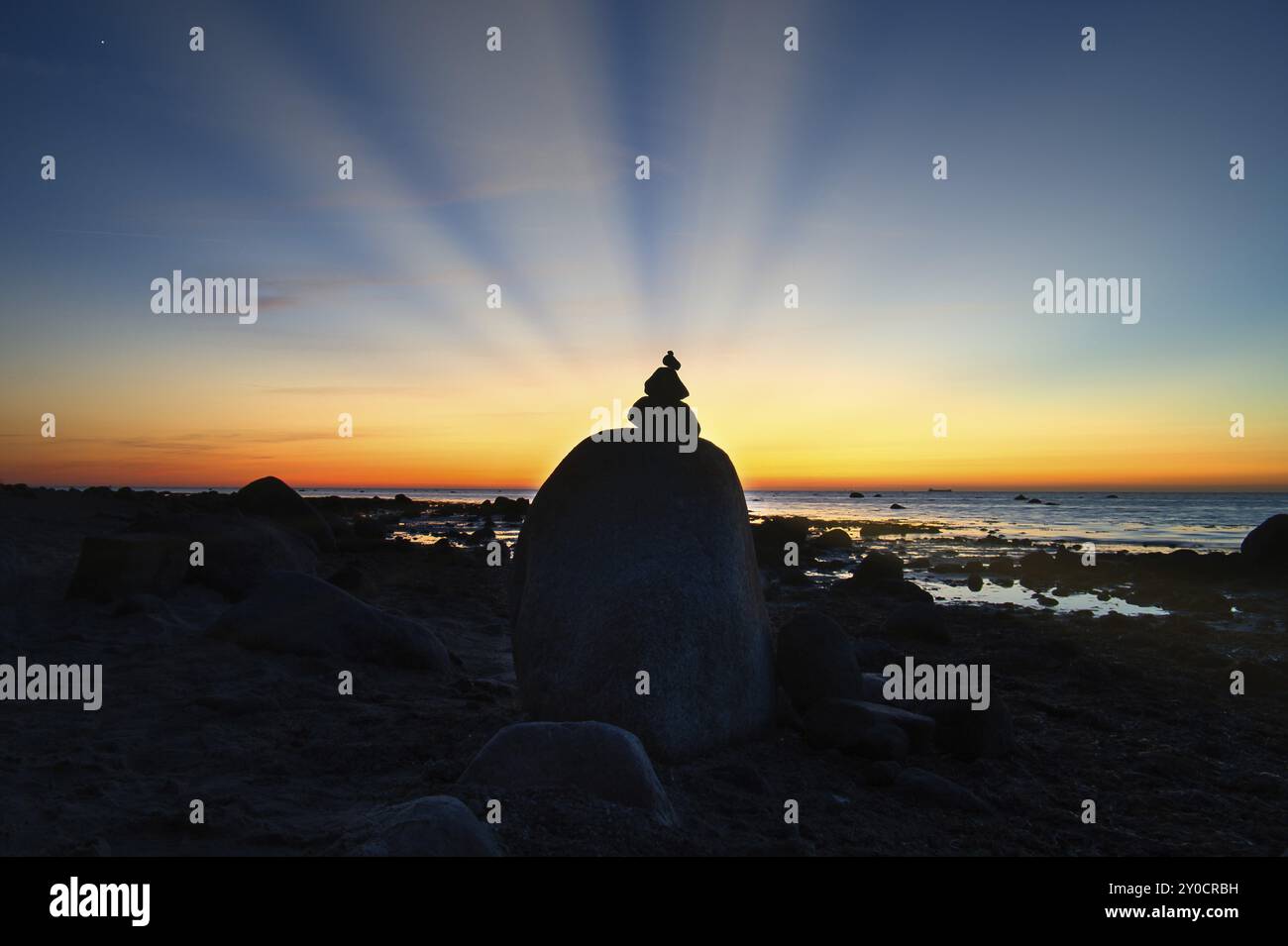 Stone pyramid on the Baltic Sea overlooking the sea at sunset. Sun shines behind stone pyramid. Stones as silhouette. Spiritual view. Landscape shot f Stock Photo