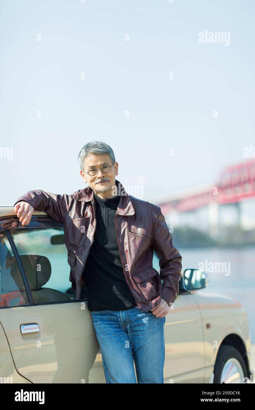 An elderly man leaning against a car at the shore Stock Photo