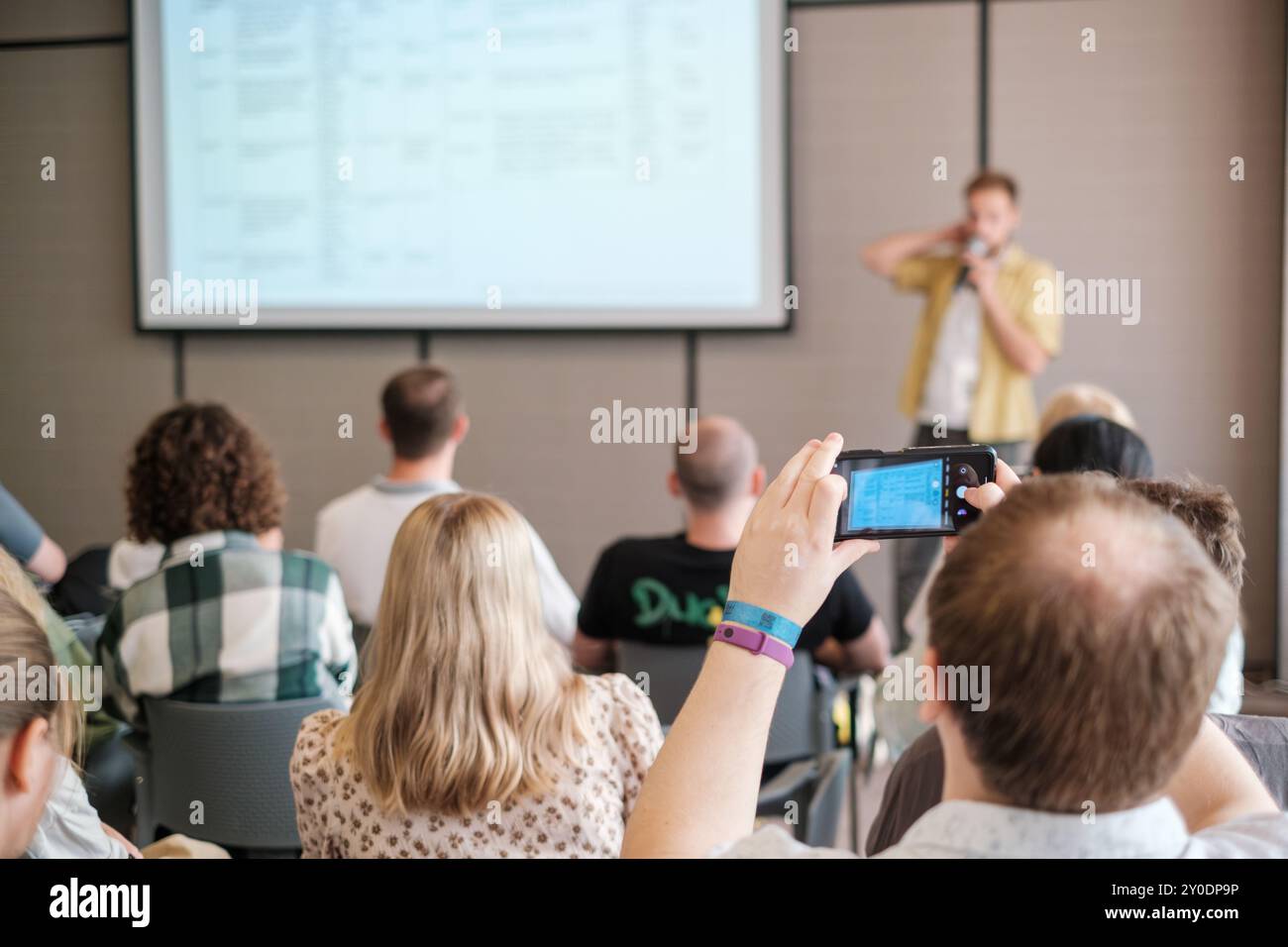 Engaged audience during a business presentation, with attendees capturing insights on mobile devices in a conference setting. Stock Photo