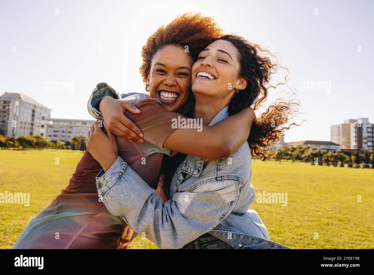 Two cheerful female students hugging in public park on a sunny afternoon, reflecting joy, friendship, and happiness. Stock Photo