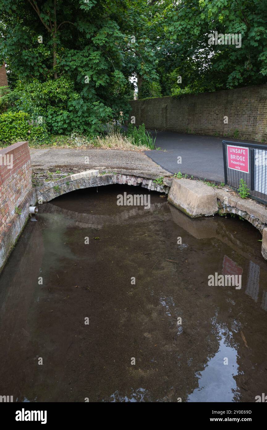 Warning sign for weak bridge at a small crumbling brick arch bridge crossing a small river Rickmansworth Hertfordshire England UK Stock Photo