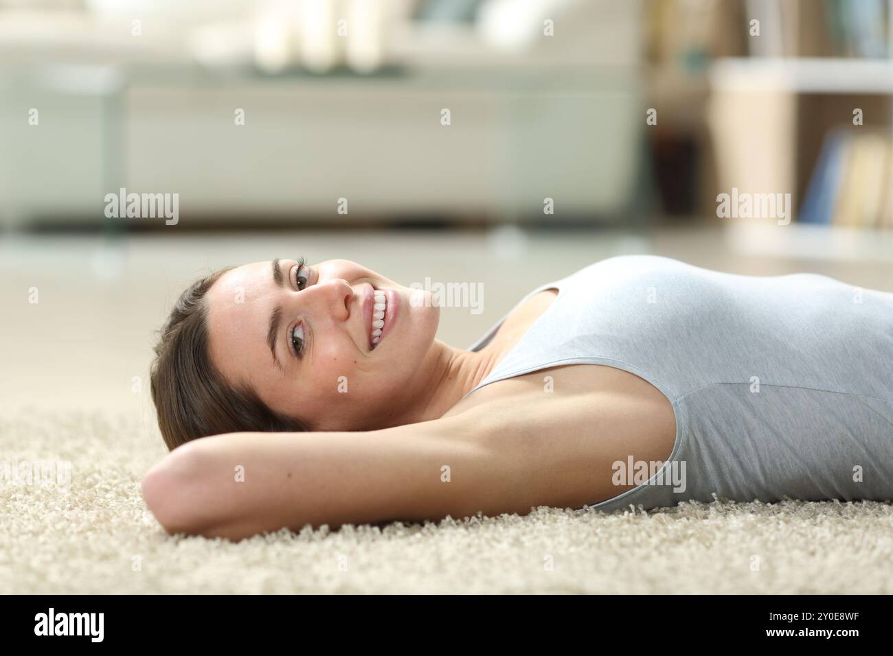 Happy woman relaxing and looking at camera with waxed oxter lying on a carpet on the floor at home Stock Photo