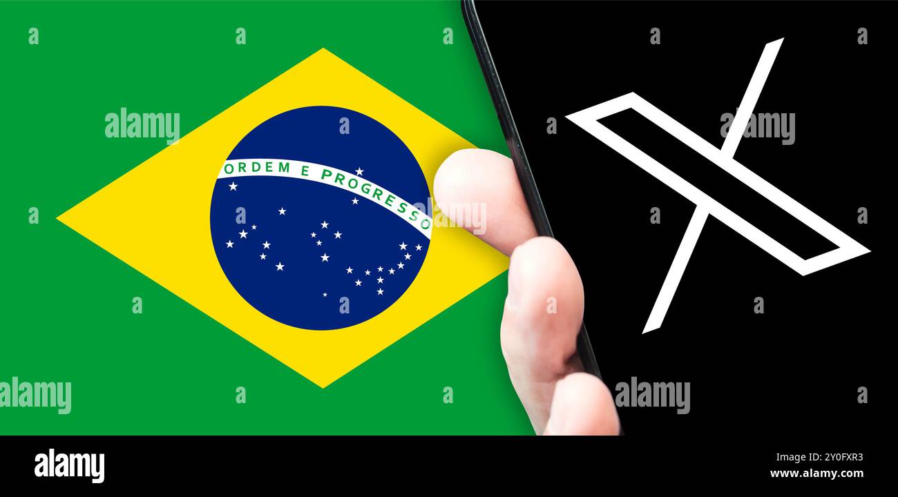 A hand holds a smartphone with the Twitter logo on the screen against the  of the Brazilian flag. Twitter X logo and Brazil flag Stock Photo